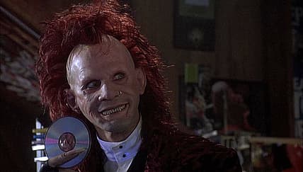 Trickster from Brainscan holding up a CD and smiling.