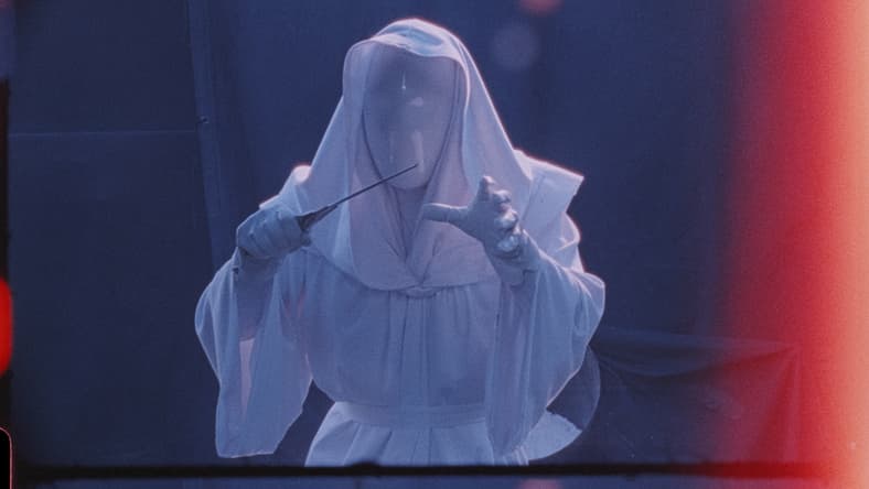A figure in a white robe, white hood, and white mask that completely obscures their face holds a knife menacingly in one hand and reaches forward with the other.