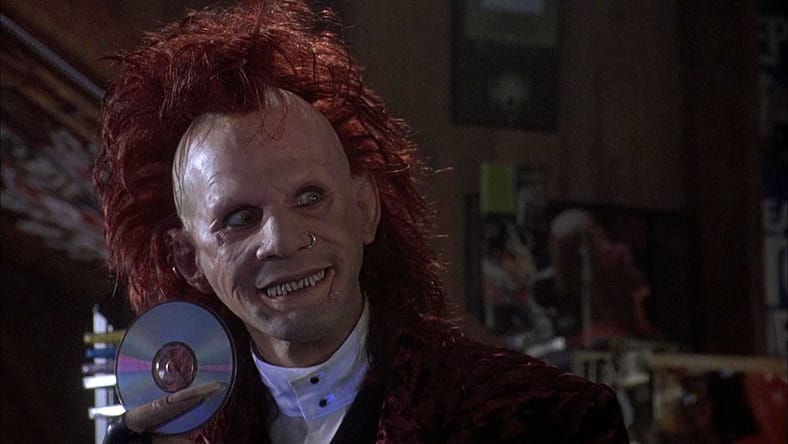 Trickster from Brainscan holding up a CD and smiling.