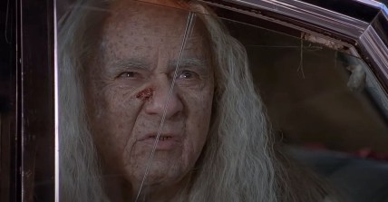 A close up an aging white haired carney with a open sore on his nose, played by Michael Constantine. looks out from a cracked car window. From the film adaptation of Stephen King's Thinner.