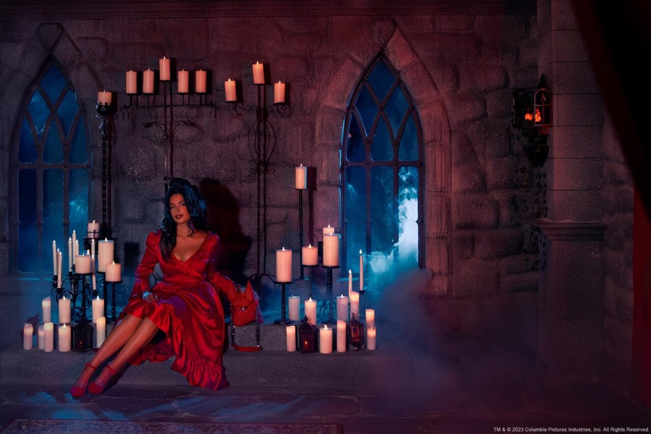 A person in a red dress sitting in front of a stone building with candles

Description automatically generated